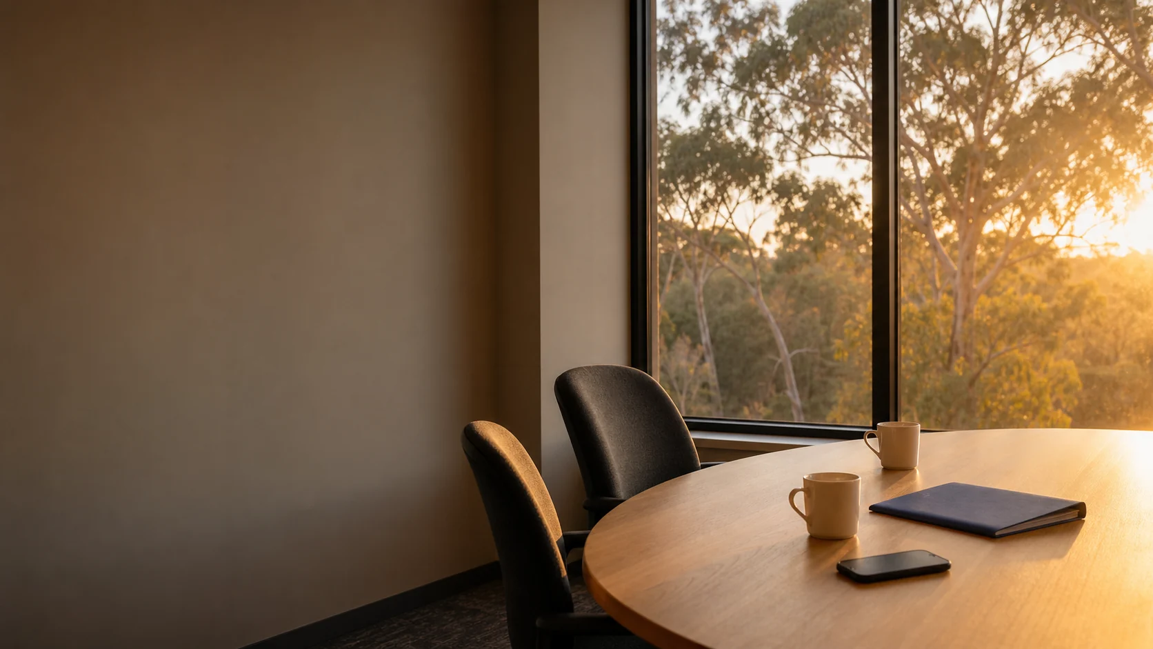 A meeting table at sunrise with two coffees, a folder and a phone