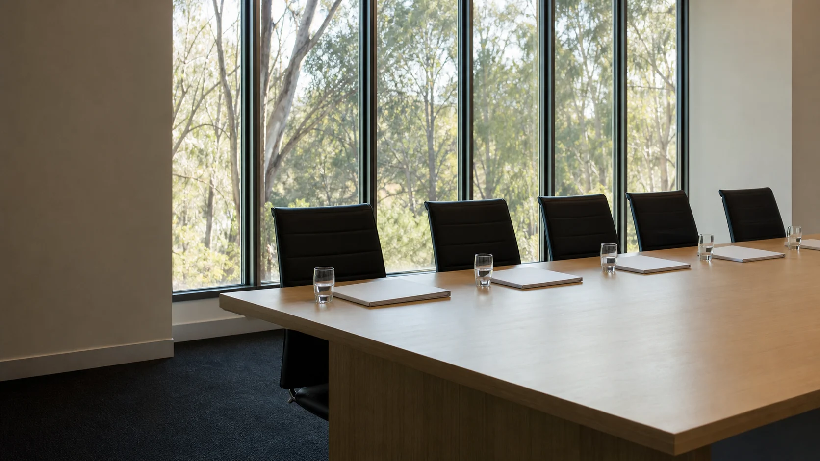 An empty meeting room with a closed folder and a glass of water at each place