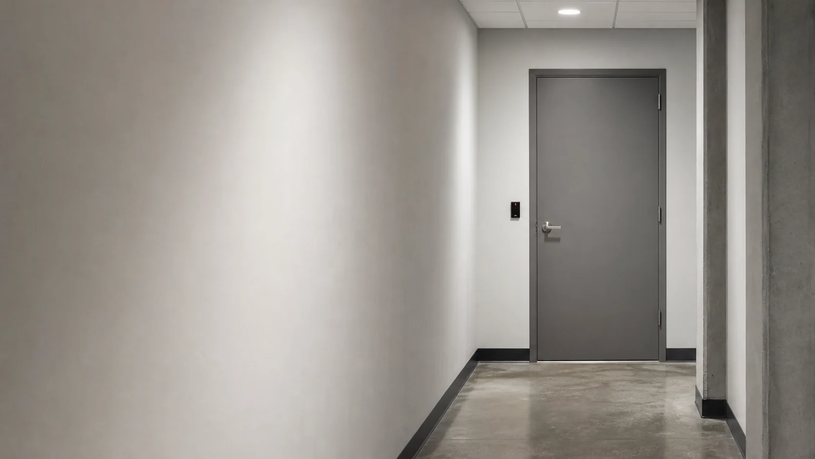 A grey steel door with a card reader at the end of a pale corridor