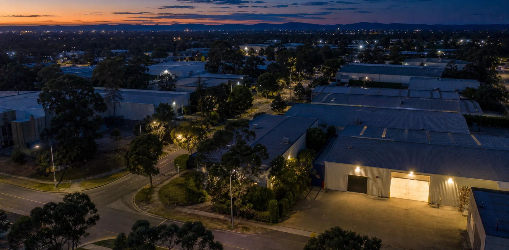 An industrial estate at dusk from the air, one roller door open and lit