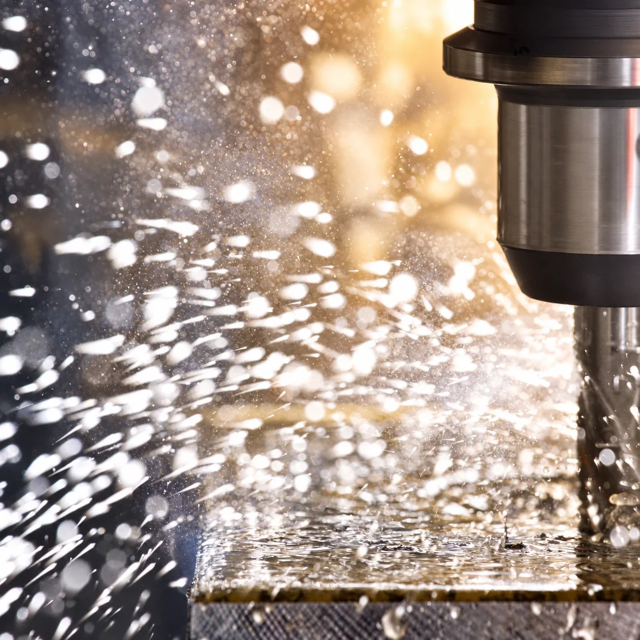 A CNC spindle cutting a steel block, coolant spraying in warm workshop light