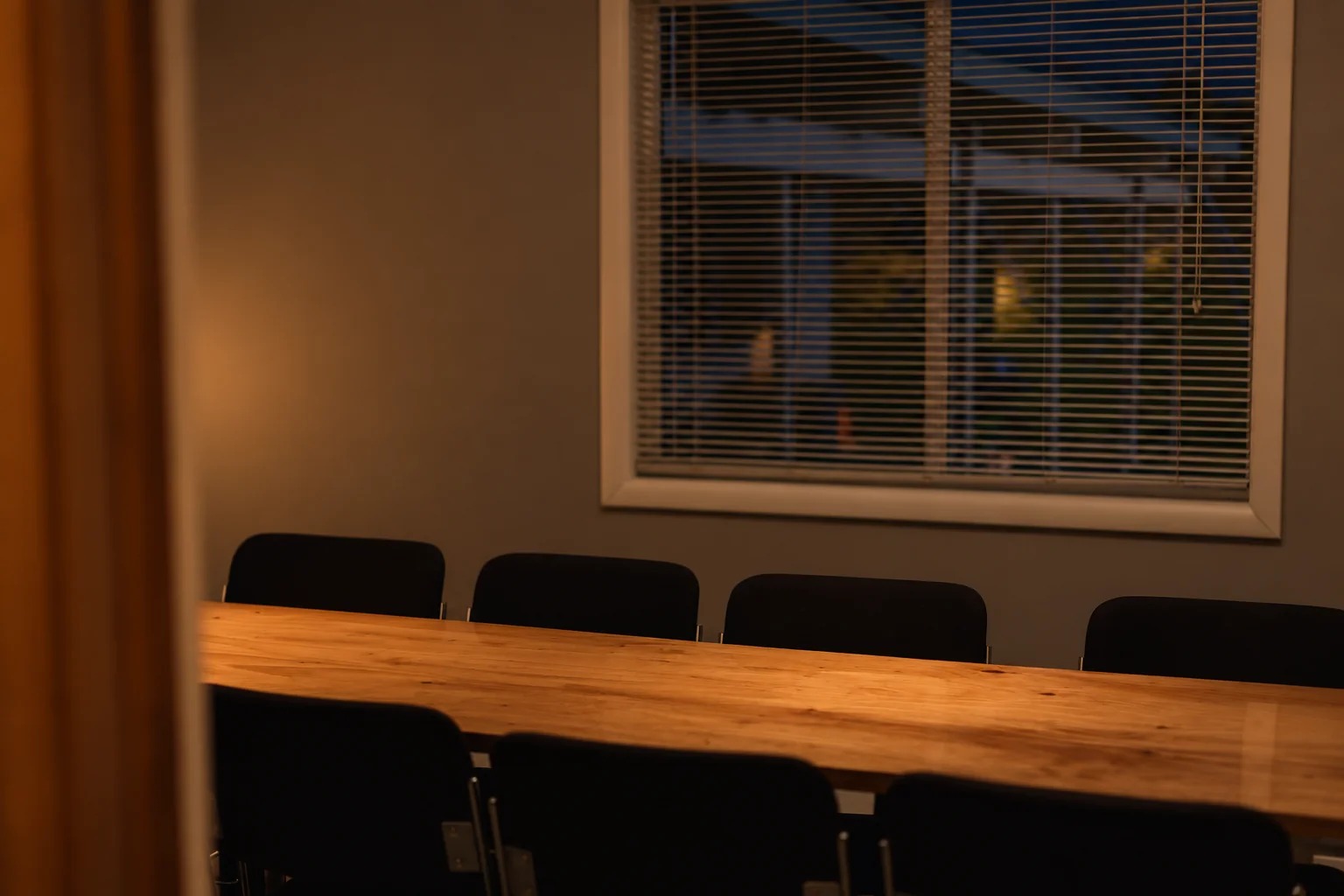 An empty boardroom after hours, a long timber table under warm light